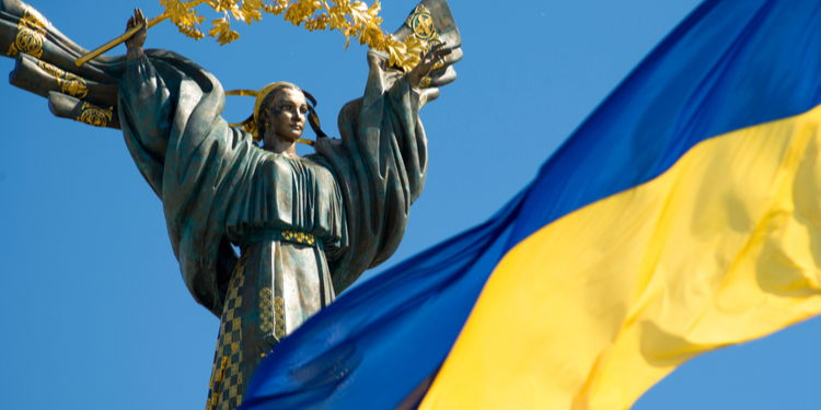 Ukrainian flag flying on sunny day with independence monument in background