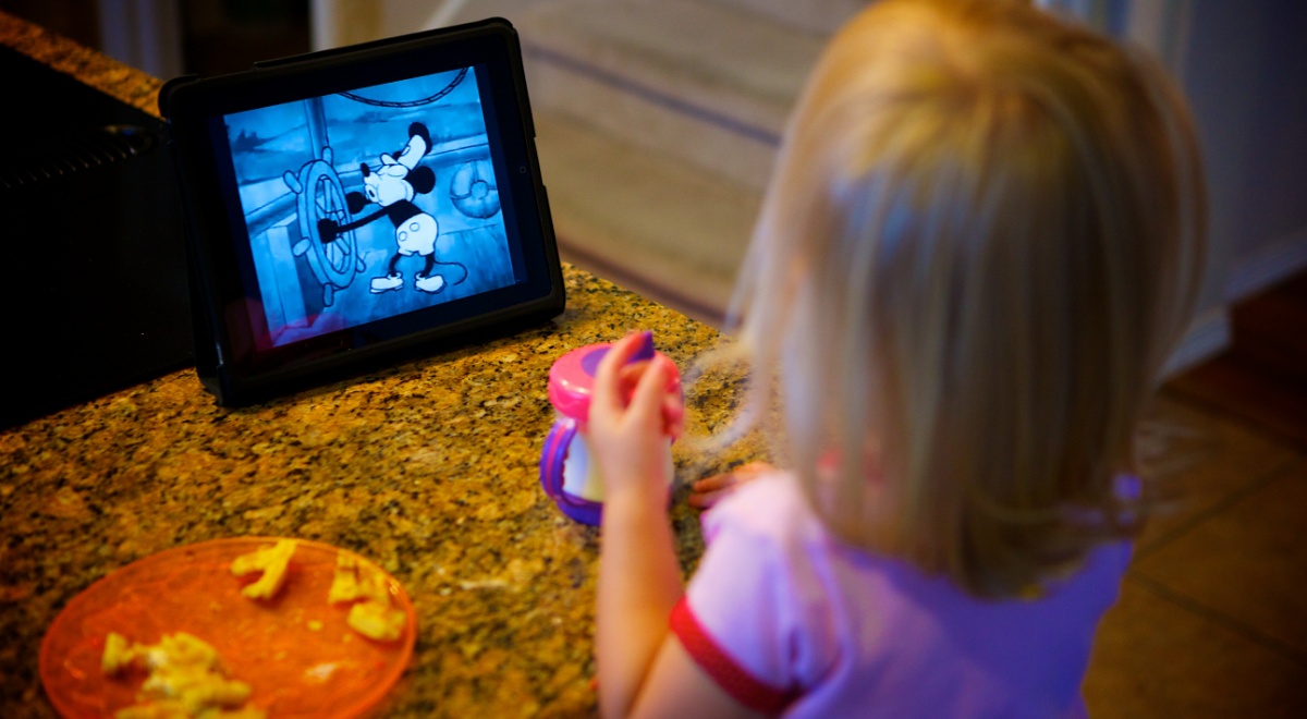 A small girl watching mickey mouse on her ipad.
