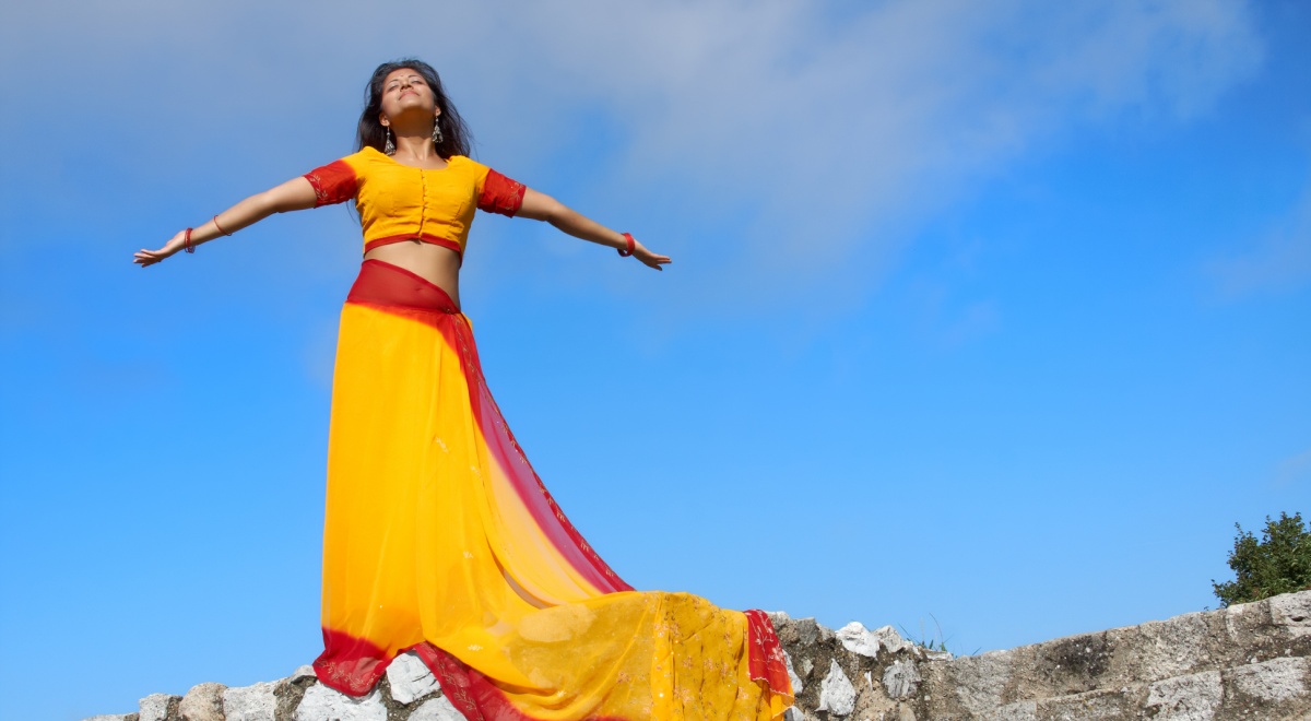 young indian woman standing on rock wall, yeallow red sari