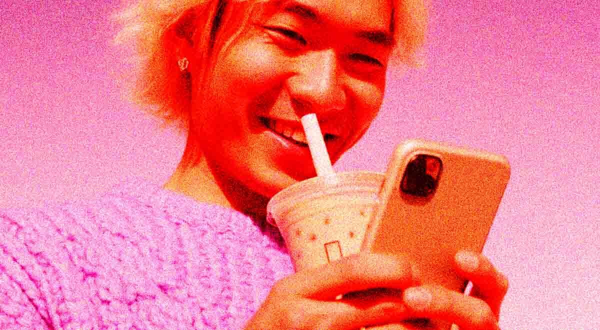 Alone young adult (Chinese) smiling at phone, milk tea nearby