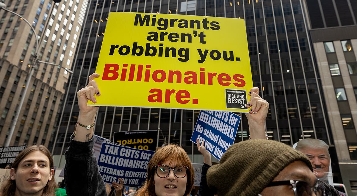 A person holding a sign that reads migrants aren't robbing you billionaires are