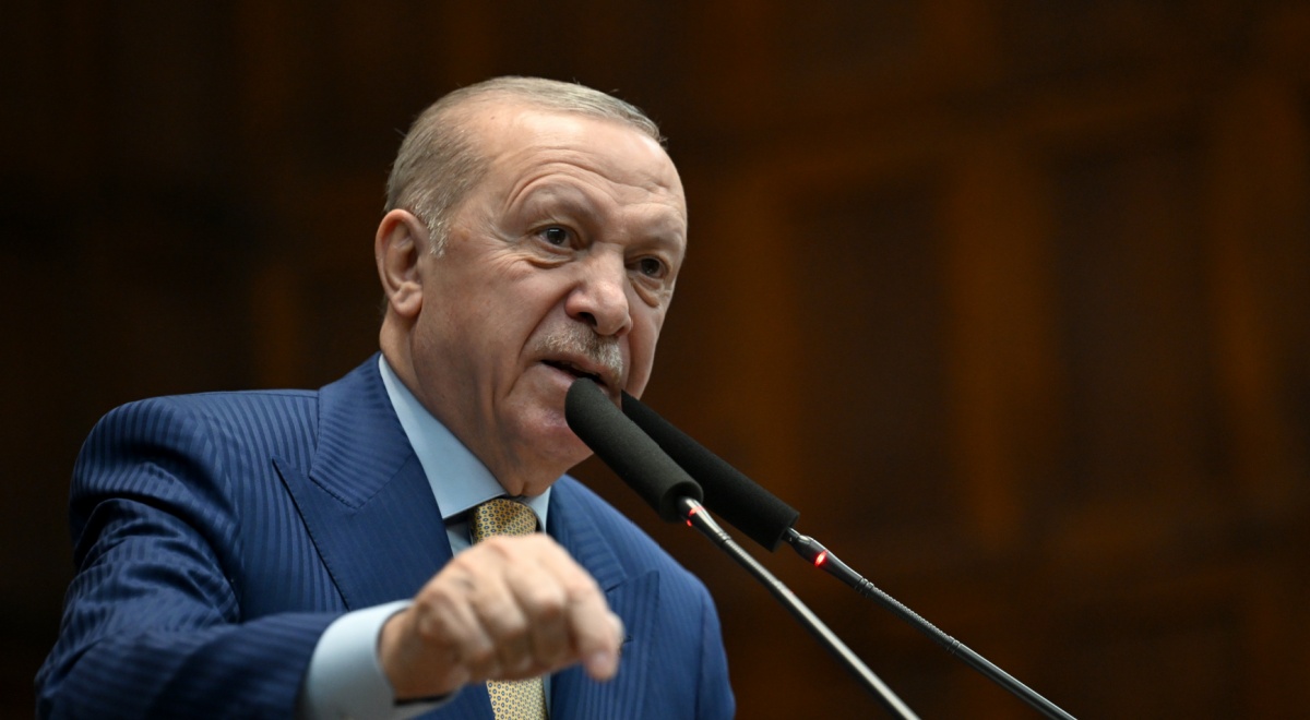 Recep Tayyip Erdogan in blue siot, baby blue shirt in front of two black vertical picrophones