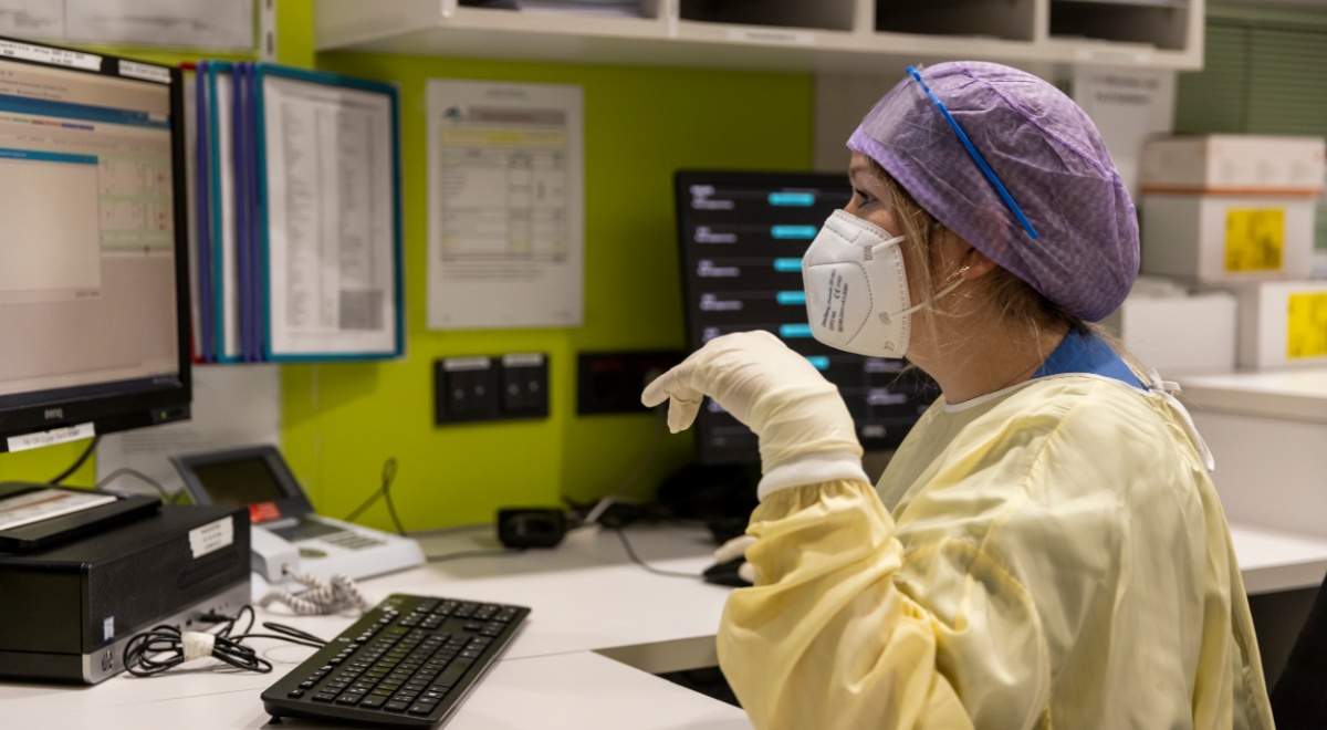 female nurse, blue har net, yellow scrub, computer monitor, white gloves, green wall