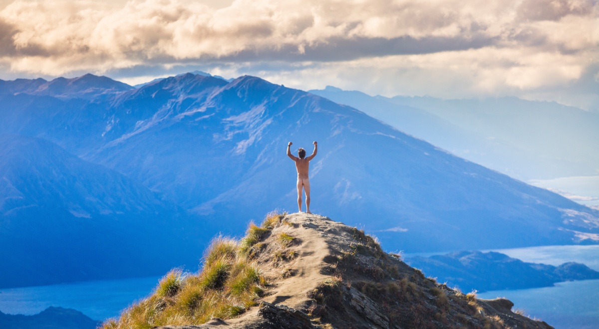 naked man on top of mountain, hands up, white clouds, grass, blue mountains, light blue sea