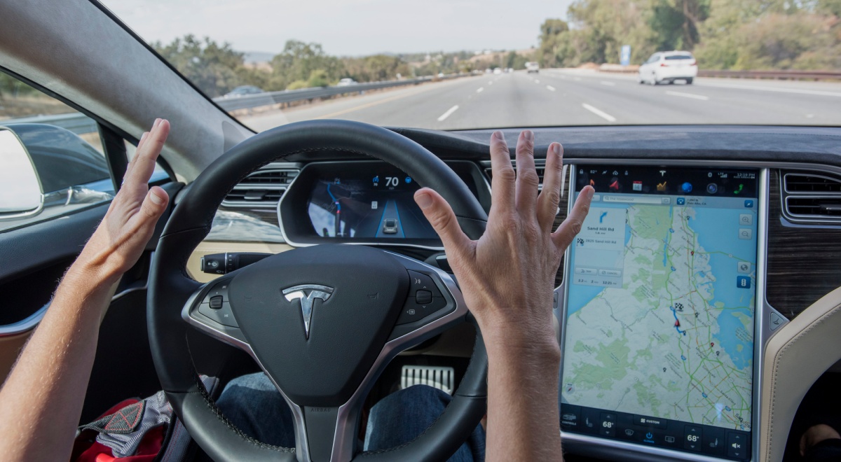tesla black driving wheel, road ahead, two white hands not touching the wheel, map on screen