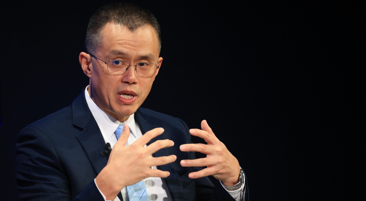 Changpeng Zhao, asian man, hands up to chest level, fingers apart, glasses, black suit, background