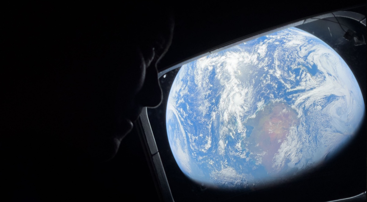 female astronaut looks from dark spacecraft cabin to blue earth in space