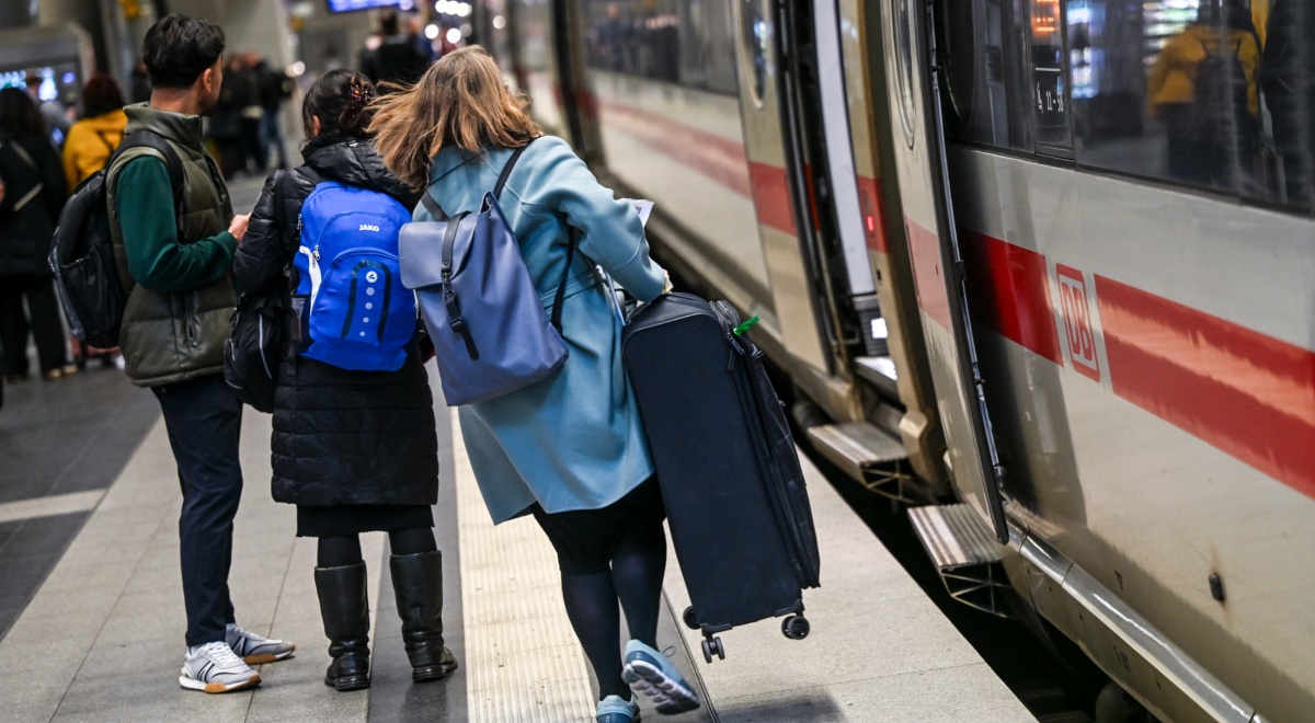 woman runs to train, open doors, long light brown hair, sky blue coat, heavy luggage