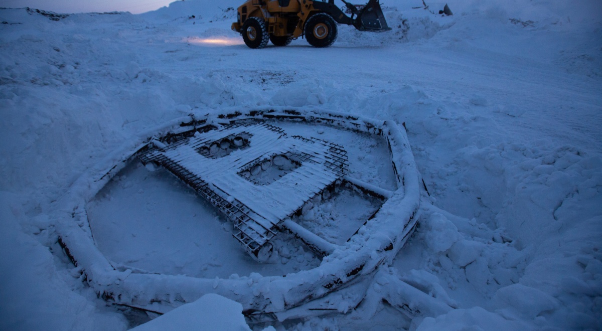 bitcoin logo sculpture made from scrap metal, frozen on snow, mining truck in the background