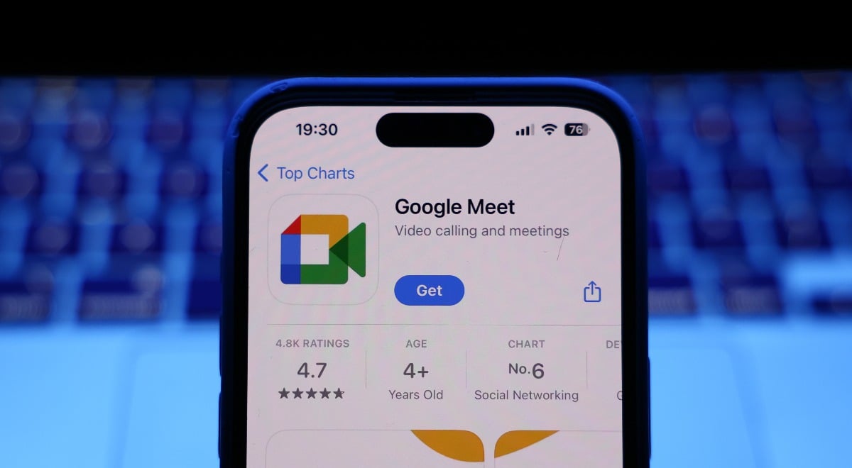 A laptop keyboard and Google Meet on App Store displayed on a phone screen