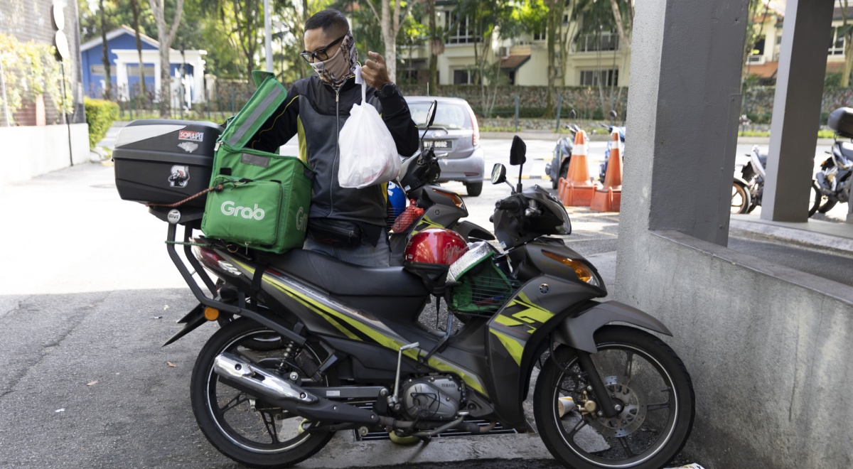 delivery driver on moped, white plastic bag, green delivery box, white GrabFood logo