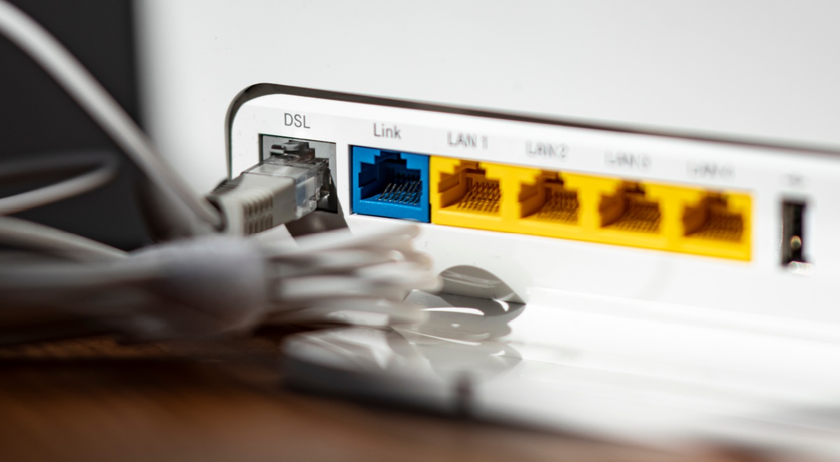 A grey LAN cable is plugged into the grey DSL slot of a white WLAN router, yellow, blue slots
