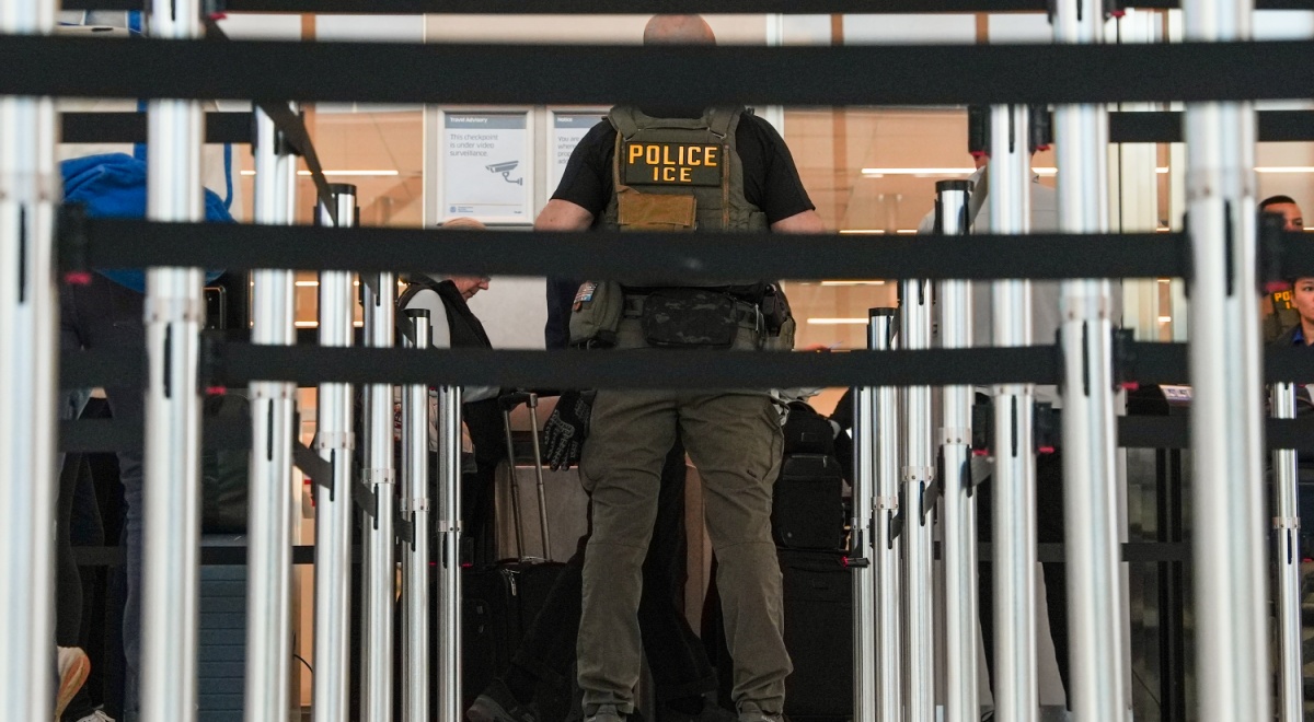 An Ice immigration agent with black security banners in front of him.