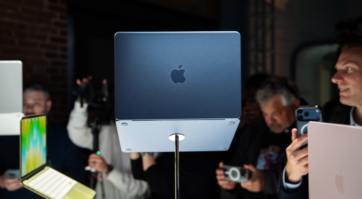 Dark grey MacBook Neo laptop computer, Asian people around it in the dark taking pictures