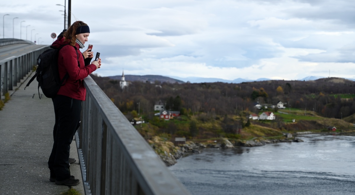 people on bridge, red jacket, maelstrom , flooded river, blue sky, white clouds, smartphone 