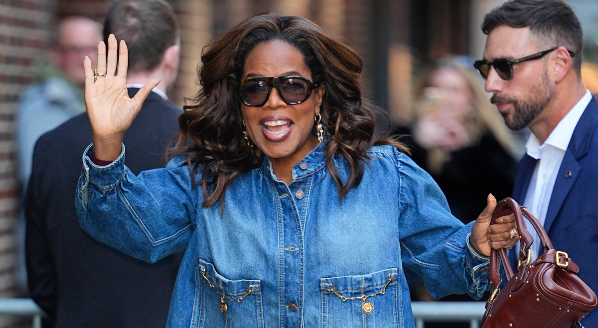Oprah Winfrey waves right hand, jeans jacket, brown purse, brown sunglasses, white man, 