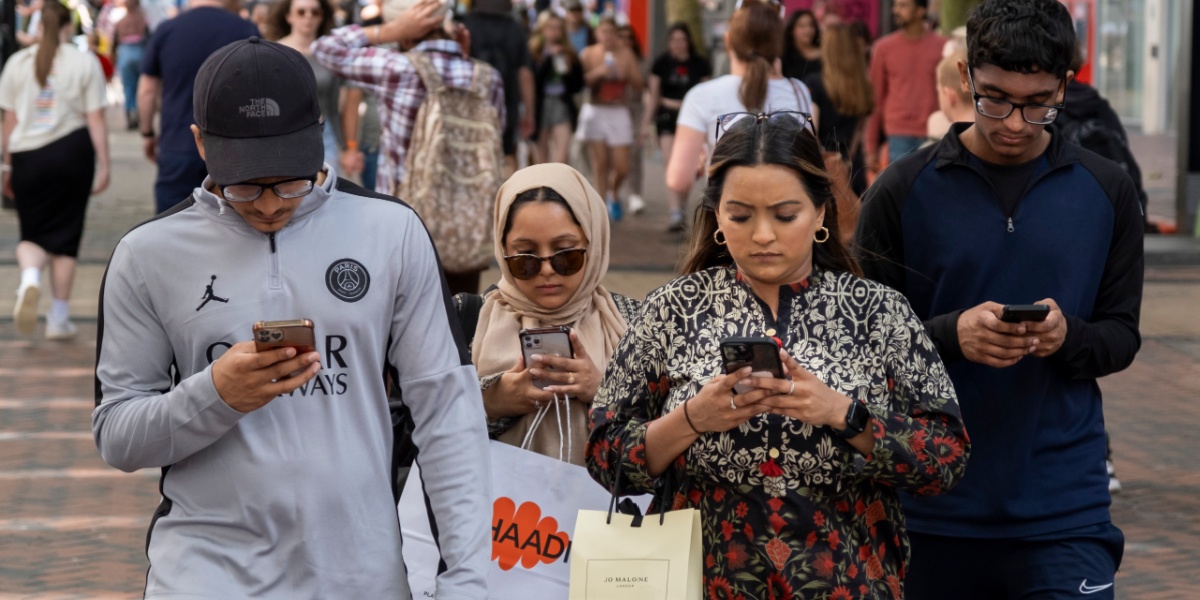 four light brown skin people, looking at smartphones, grey shirt, paper shopping bags, sunglasses