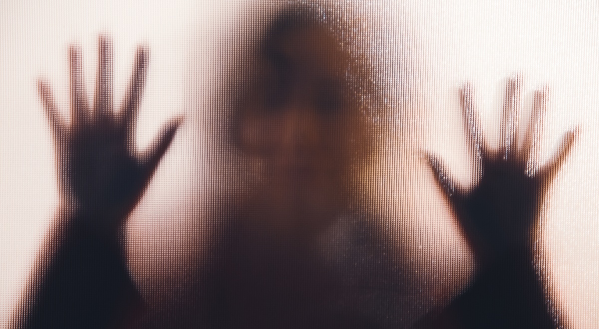 A shadow of a rape victim behind glass.