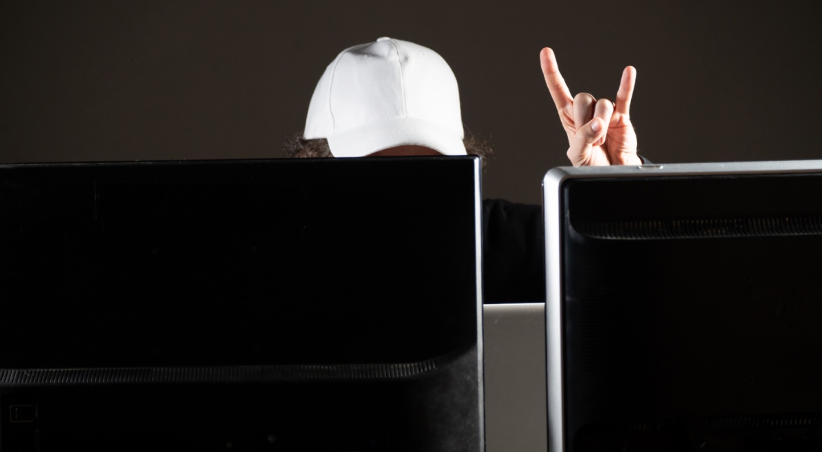 white baseball hat on head behind two black screens, rock and roll fingers in the air
