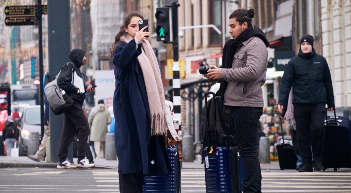 male and female tourists, darker skin, black smartphone, two dark blue luggages, pedestrian