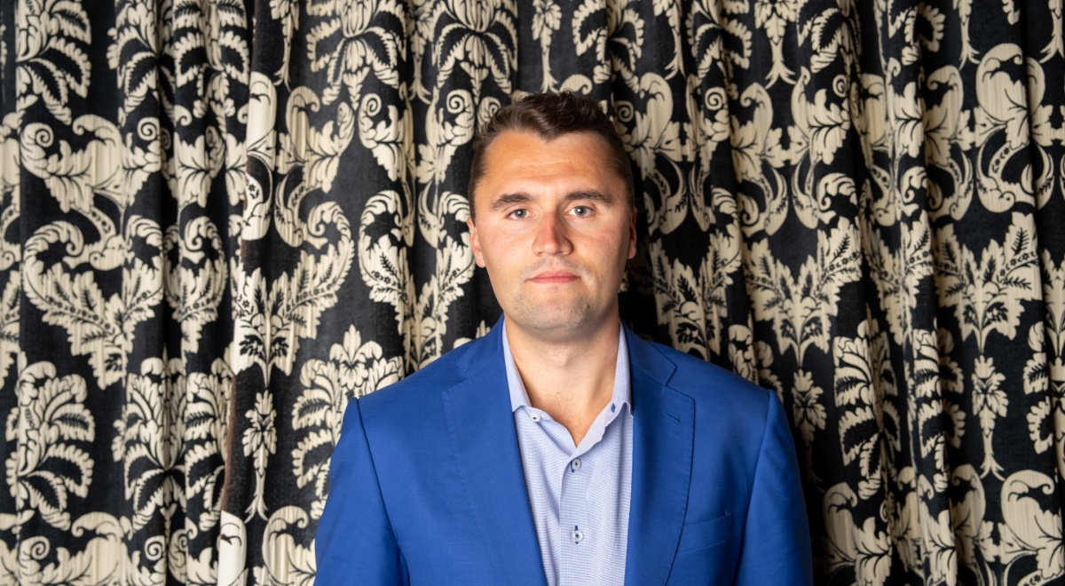 Charlie Kirk standing in front of a decorative curtain.
