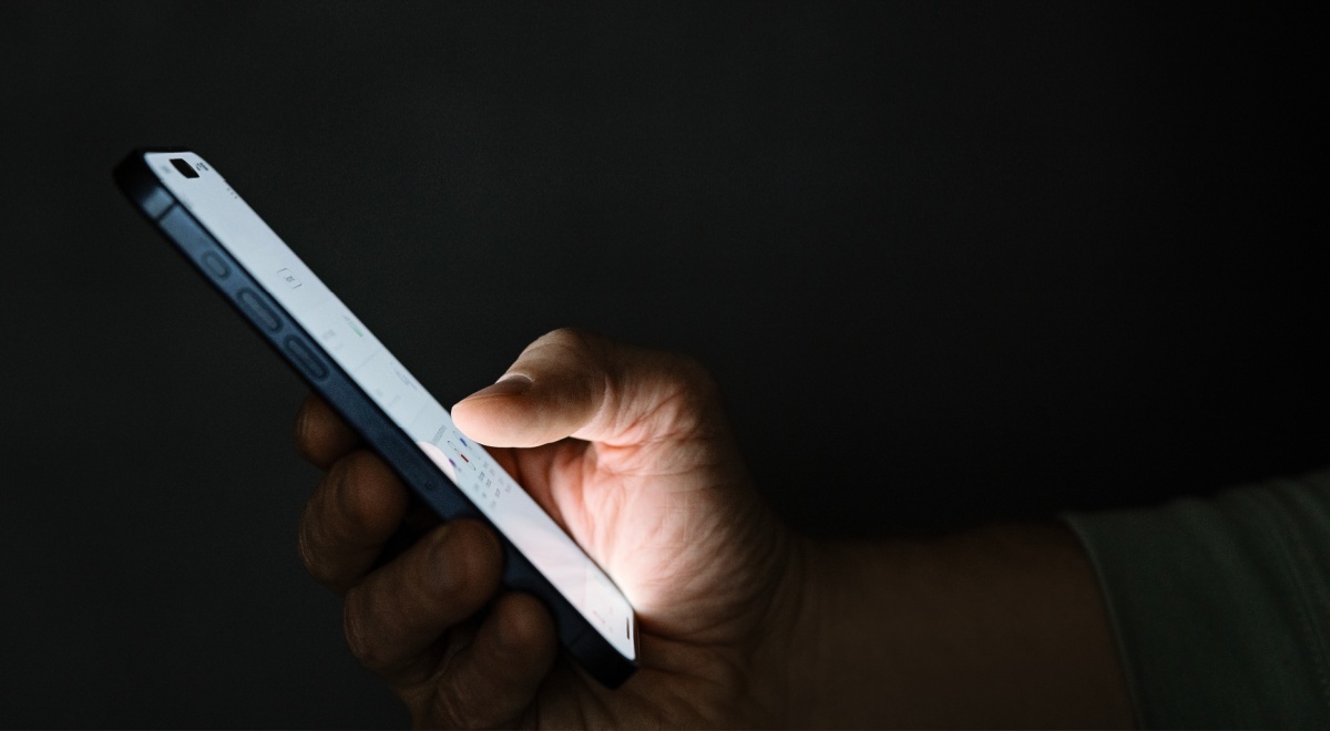 white phone screen held inright hand, shown from profile, dark room