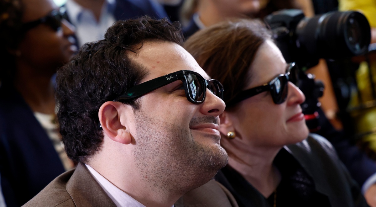white man, chubby cheeks, dark curly hair, smiling, black ray-ban sun glasses, white woman