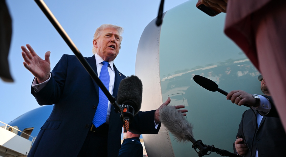 donald trump, bright blue tie, white shirt, sea blue plane turbine, black microphones, clear sky