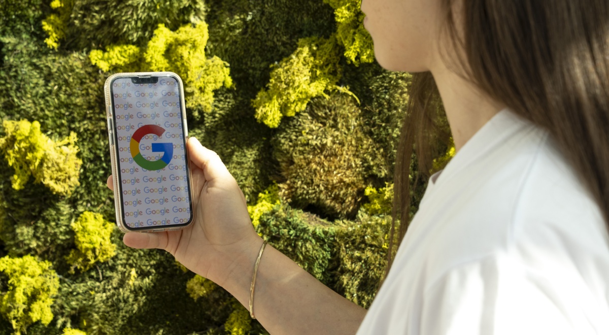 Google logo on white smartphone screen, white t-shirt, white female, long dark brown hair, green