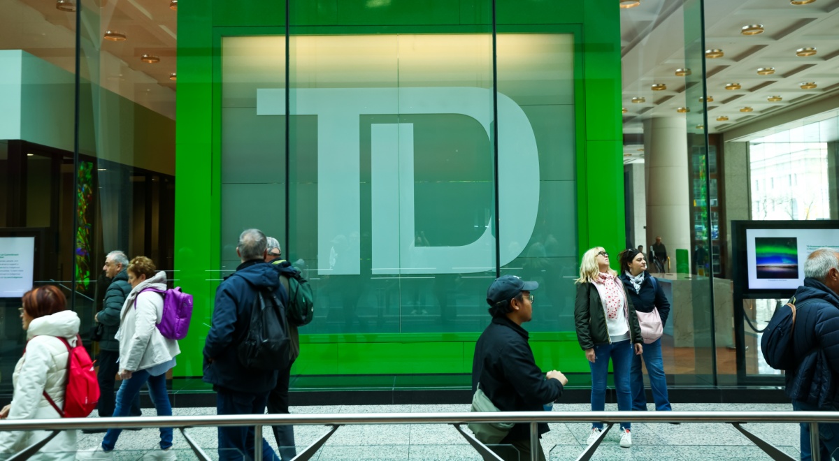 TD bank logo in green behind glass wall, about ten pedestrians walking in warm clothes