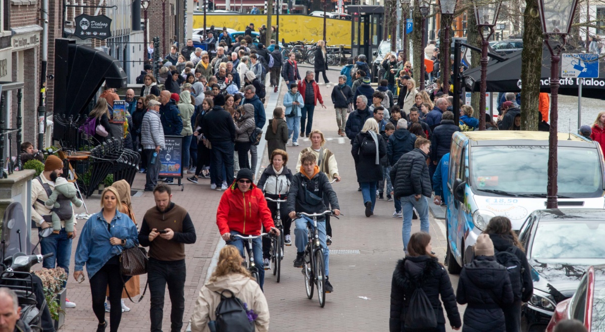 busy street filled with white pedestrians, cyclists, red jacket, water canal, blue jeans jacket