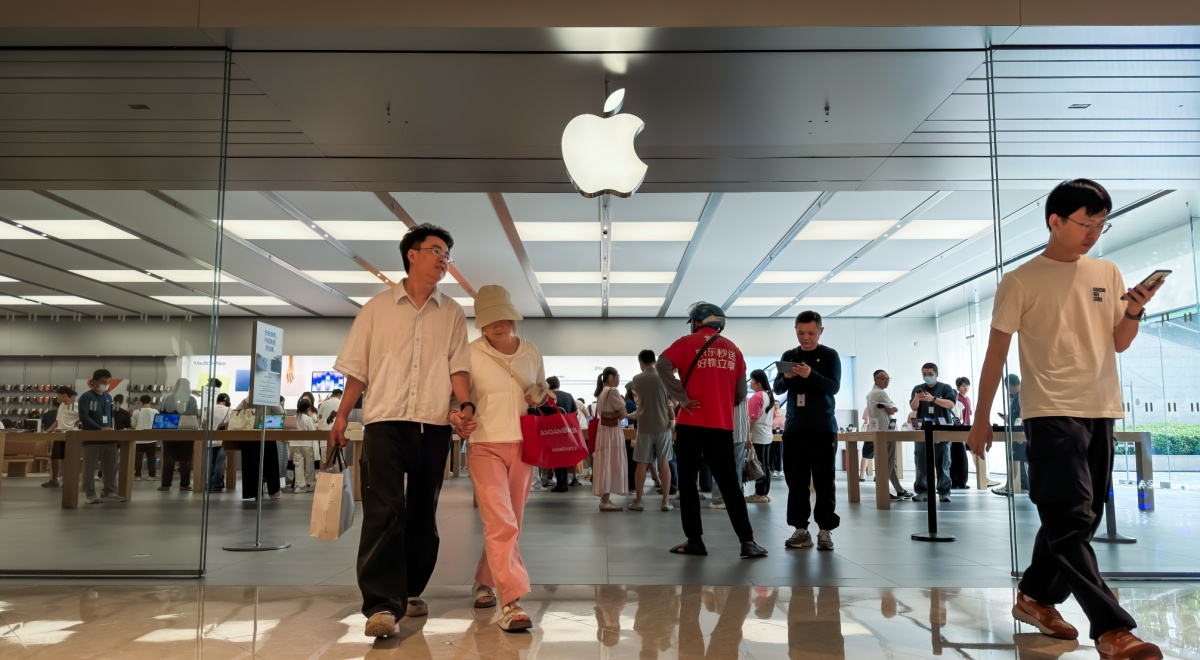 middle aged white asian couple exit apple store, logo, pink pants, black hair, glass wall, white tshirt