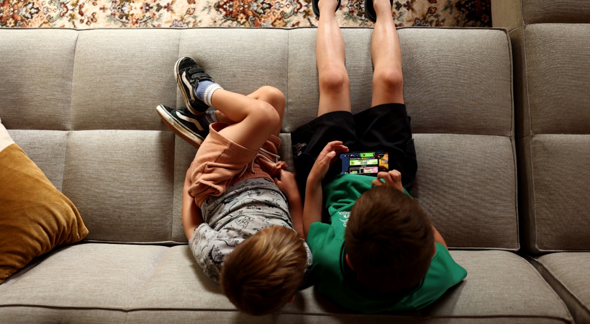 two white boys, green t-shirt- black shorts, grey t-shirt, light grey sofa, roblox on iphone screen