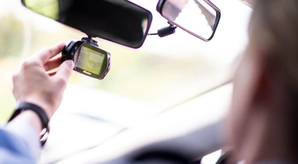 black dash camera attached to rear view window, white male hand, baby blue sleeve