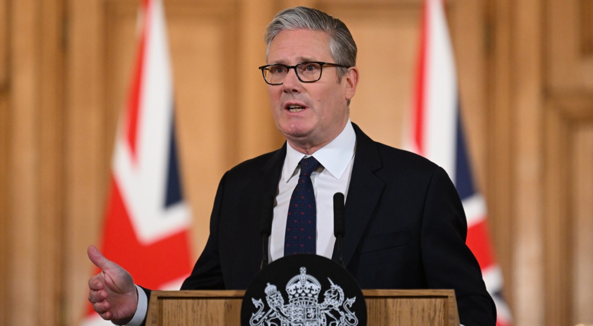 keir starmer, black suit, two UK flags, dark tie, white collar shirt,