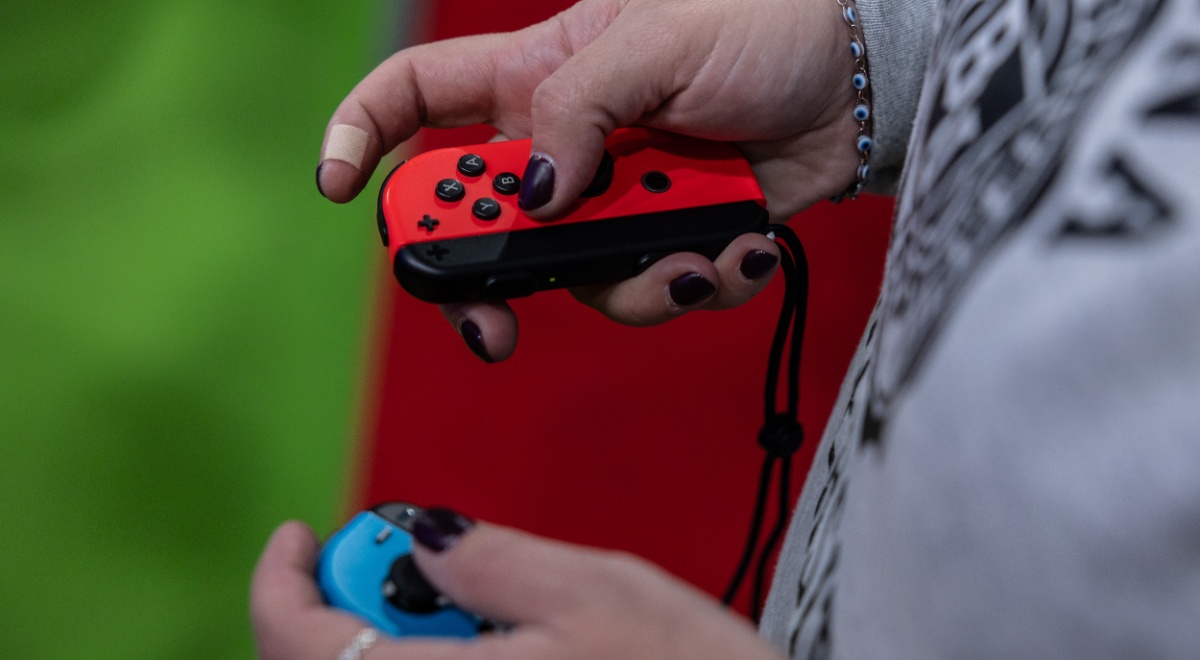 nintendo joy con held in white female hands, grey jumper, grass green background