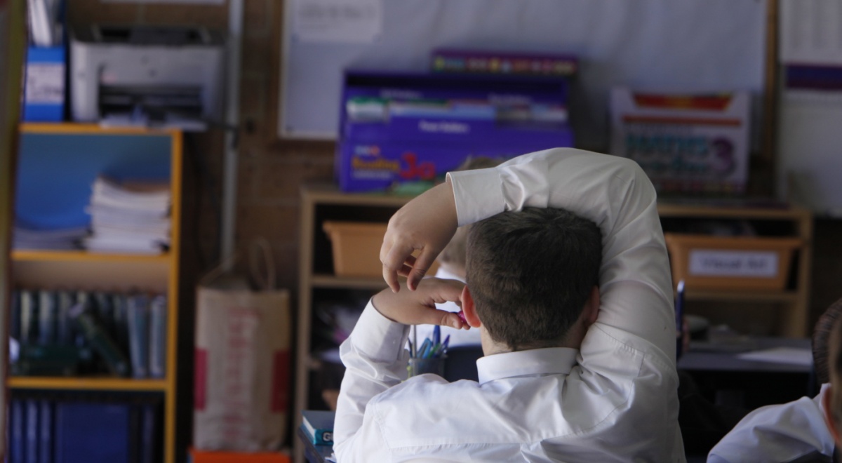 white male school boy in classroom, white collar shirt, right hand over head, light hair
