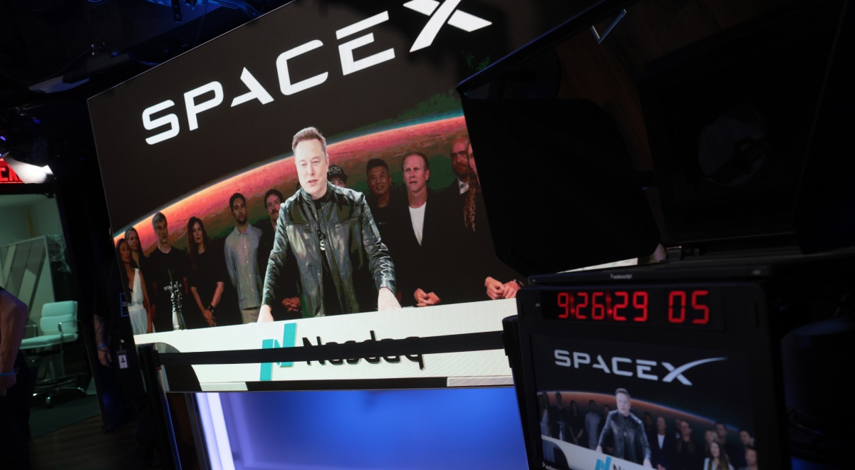 spaceX logo, elon musk on big screen, taking in video, black jacket, nasdaq