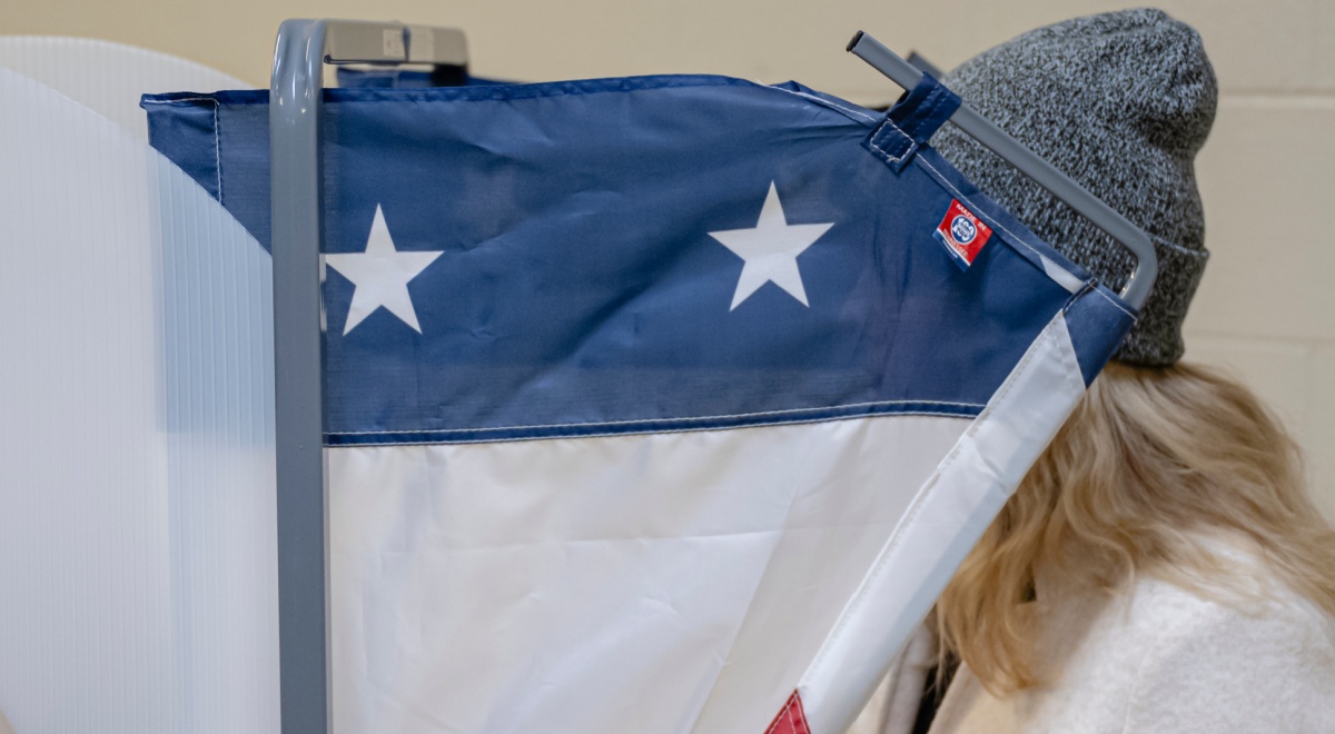 voting machine, blue and two white stars, blonde hair, dark grey beany hat, white jumper