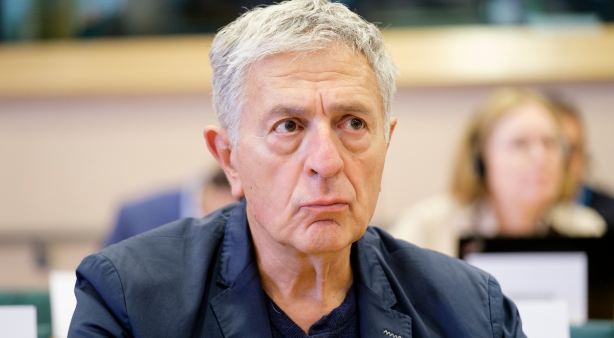 Stelios Kouloglou, white elder greek man, black collar shirt, no tie, grey hair, dark blazer,