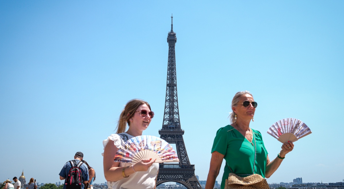eiffel tower, clear blue sky, two white females, blonde, folding fans, green t-shirt, sunglasses
