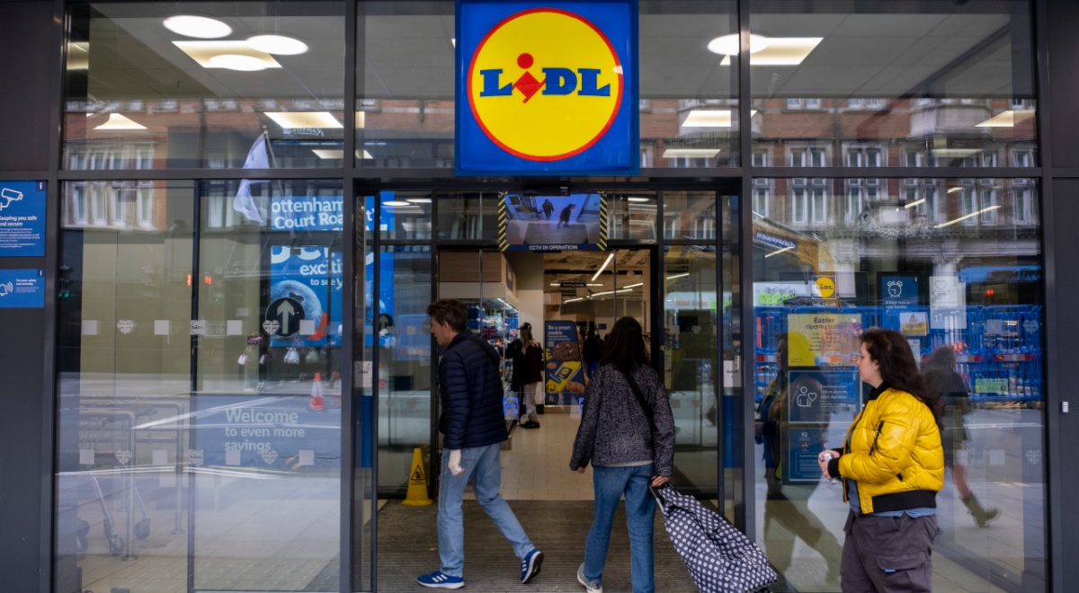 lidl store, glass wall and door, white woman in padded yellow winter jacket, shopping cart