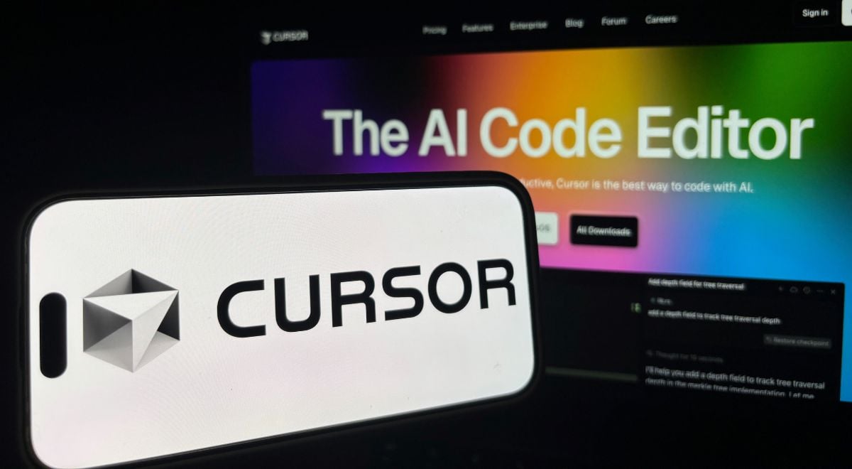 Cursor logo on phone, background AI coding agent written on computer screen.