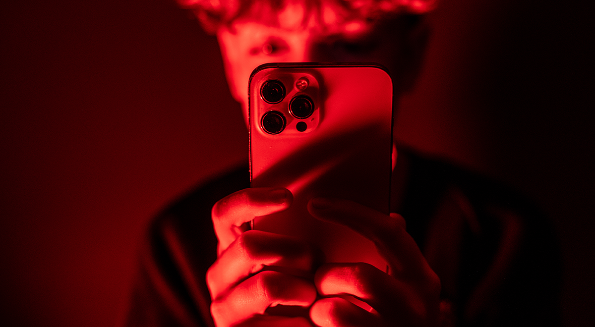 teenage boy looks at an iPhone screen displaying various social media apps in red background