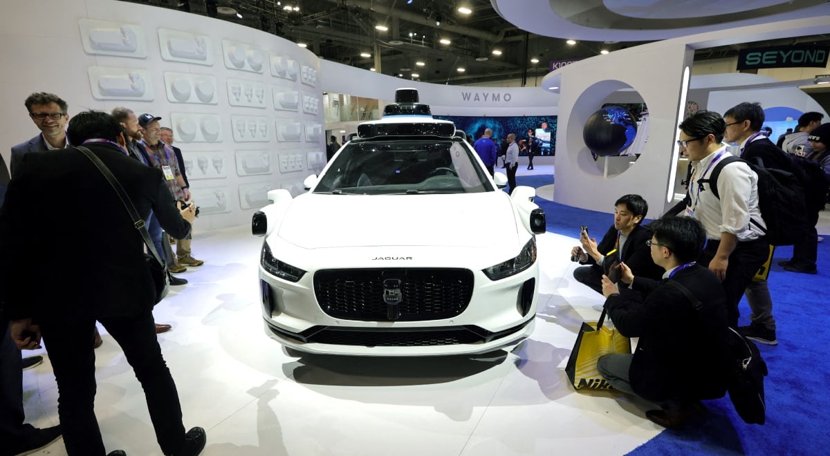 white Jaguar car on white pedestal, people around in black outfits take pictures of it 