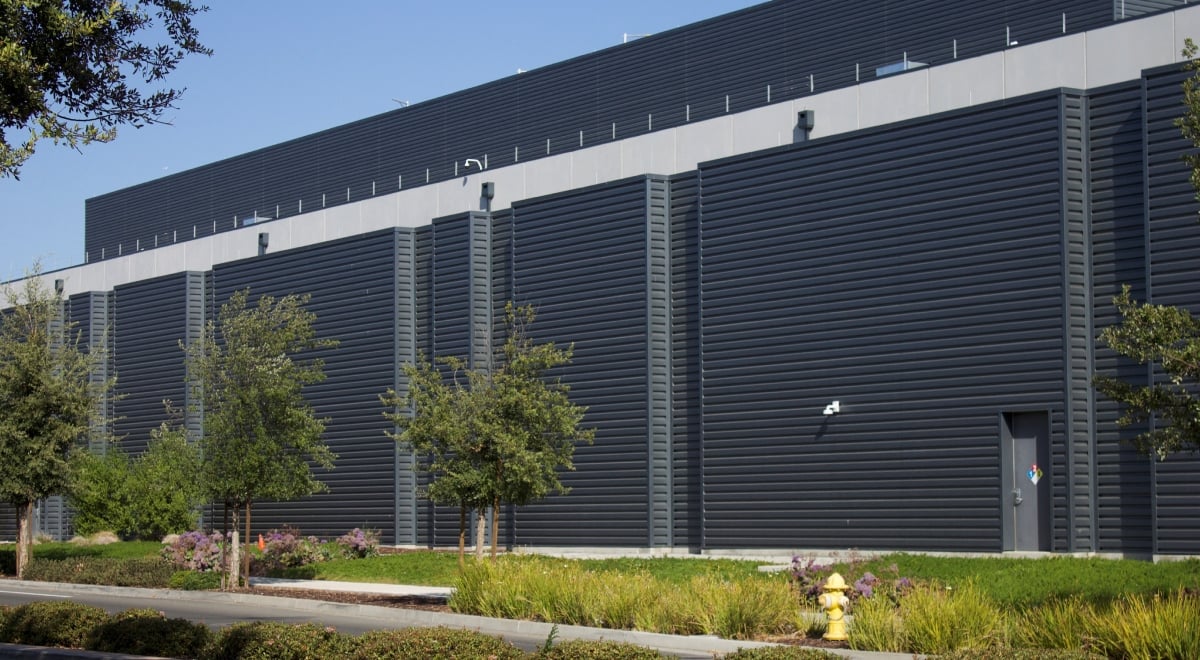 dark grey ai data centre building, some green grass, blue sky, five trees