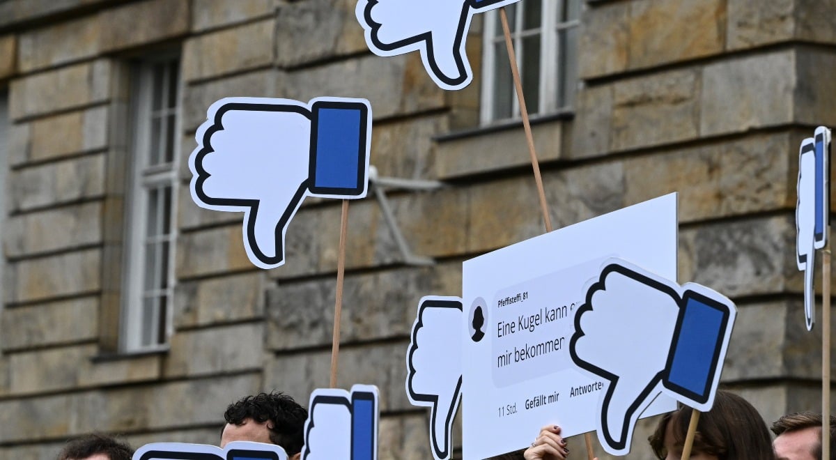 Protesters in Germany stand with their Facebook thumbs pointing down posters