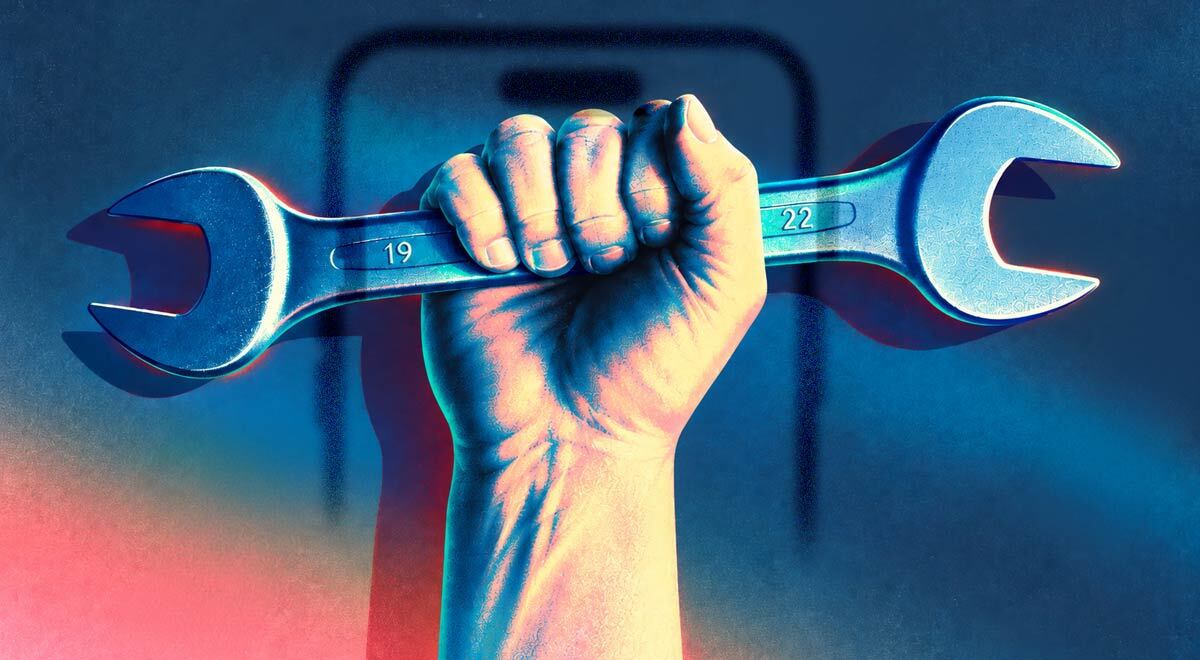 A hand holding a wrench with a smartphone in the background