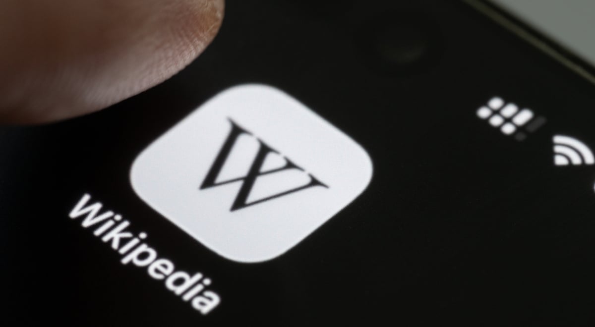 Finger press Wikipedia app icon close up view on smartphone screen