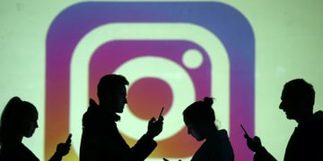 Silhouettes of mobile users are seen next to a screen projection of the Instagram logo